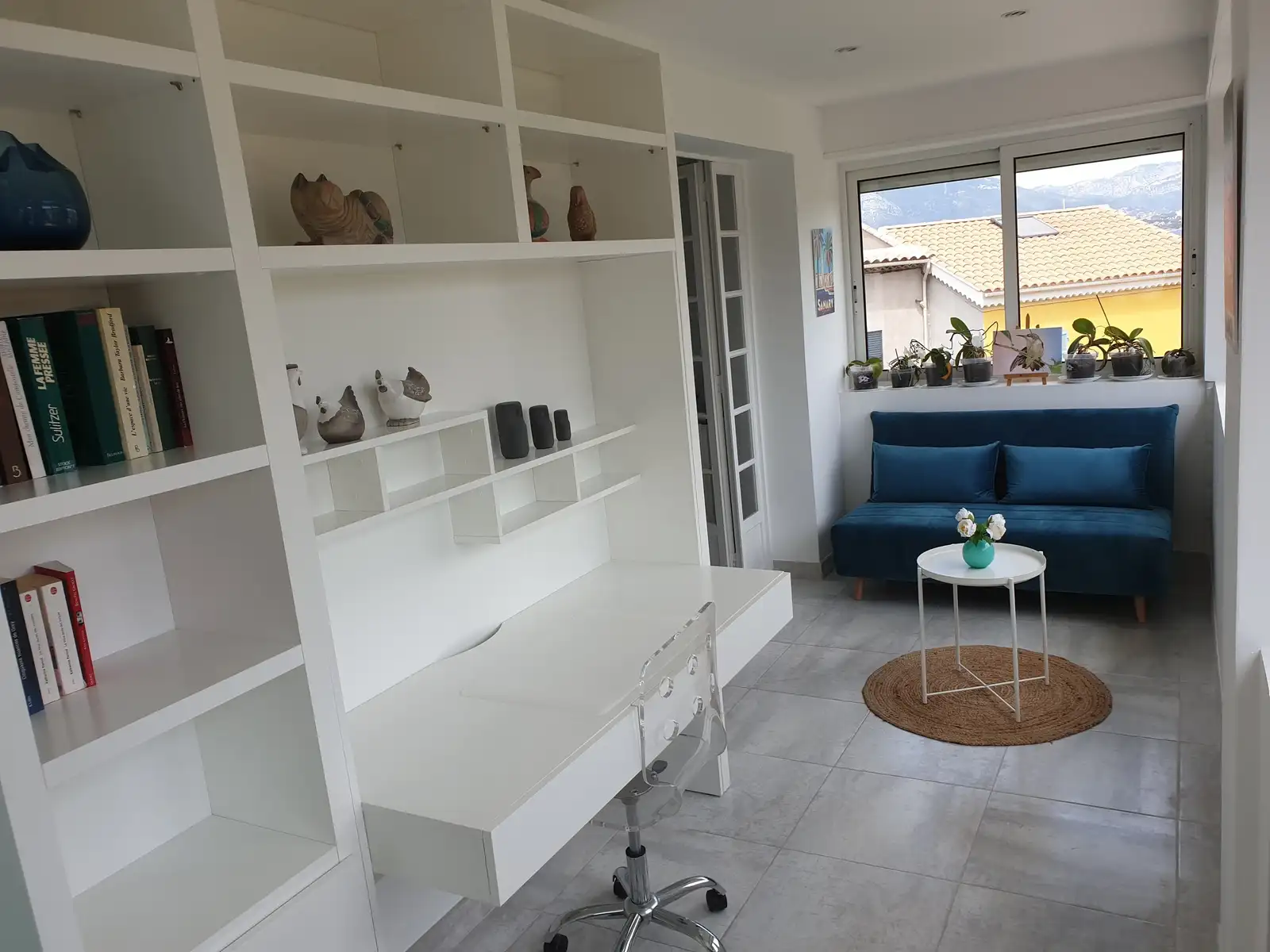 Espace bureau avec étagères, plan de travail et canapé près de la fenêtre