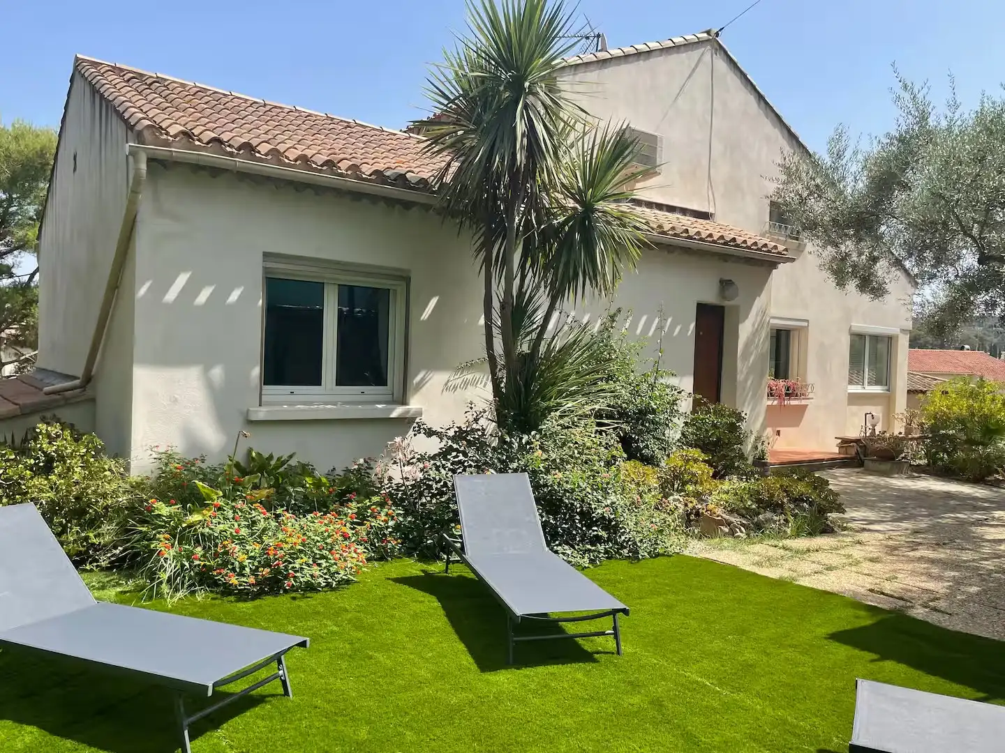 Façade de Villa Le Colibri côté jardin, palmier et transats sur la pelouse