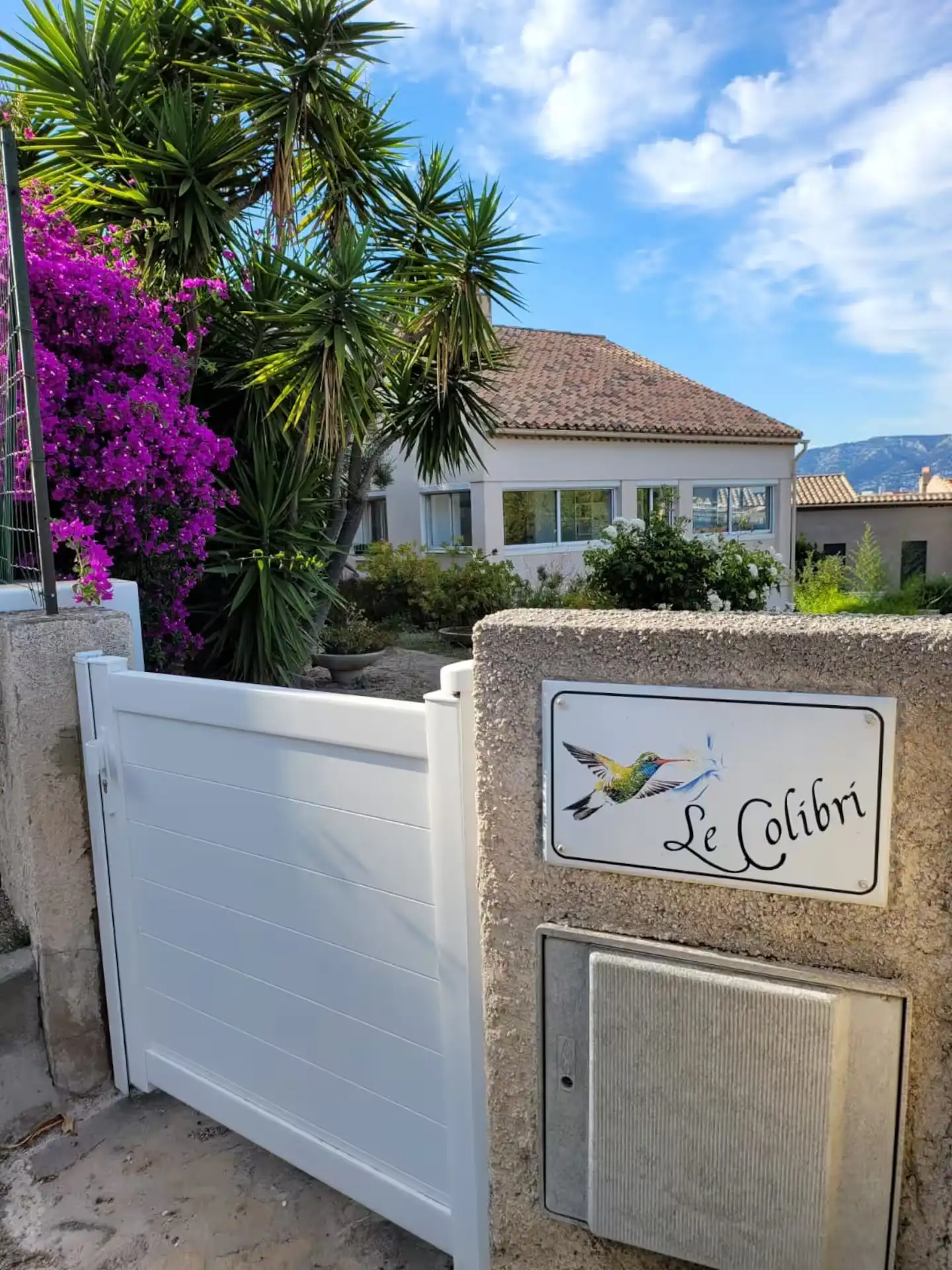 Portail de la maison avec la plaque « Le Colibri » et des bougainvilliers